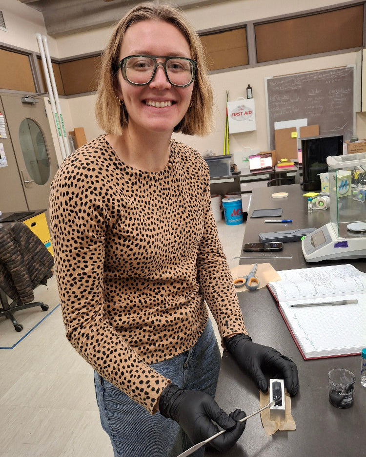 Engineer wearing a leopard print shirt and black gloves holding a device in an indoor lab setting.
